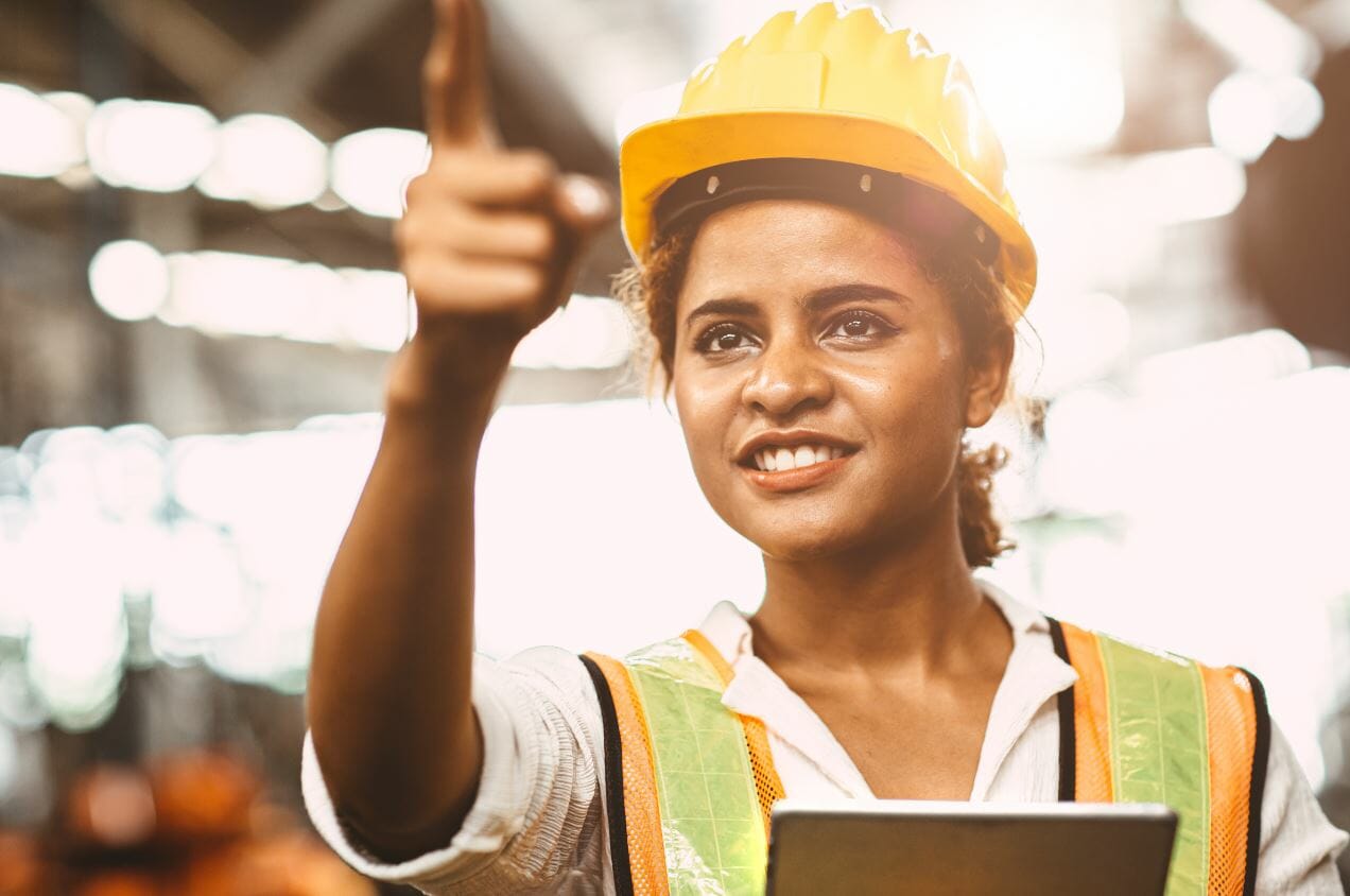 Woman in hard hat pointing in a warehouse