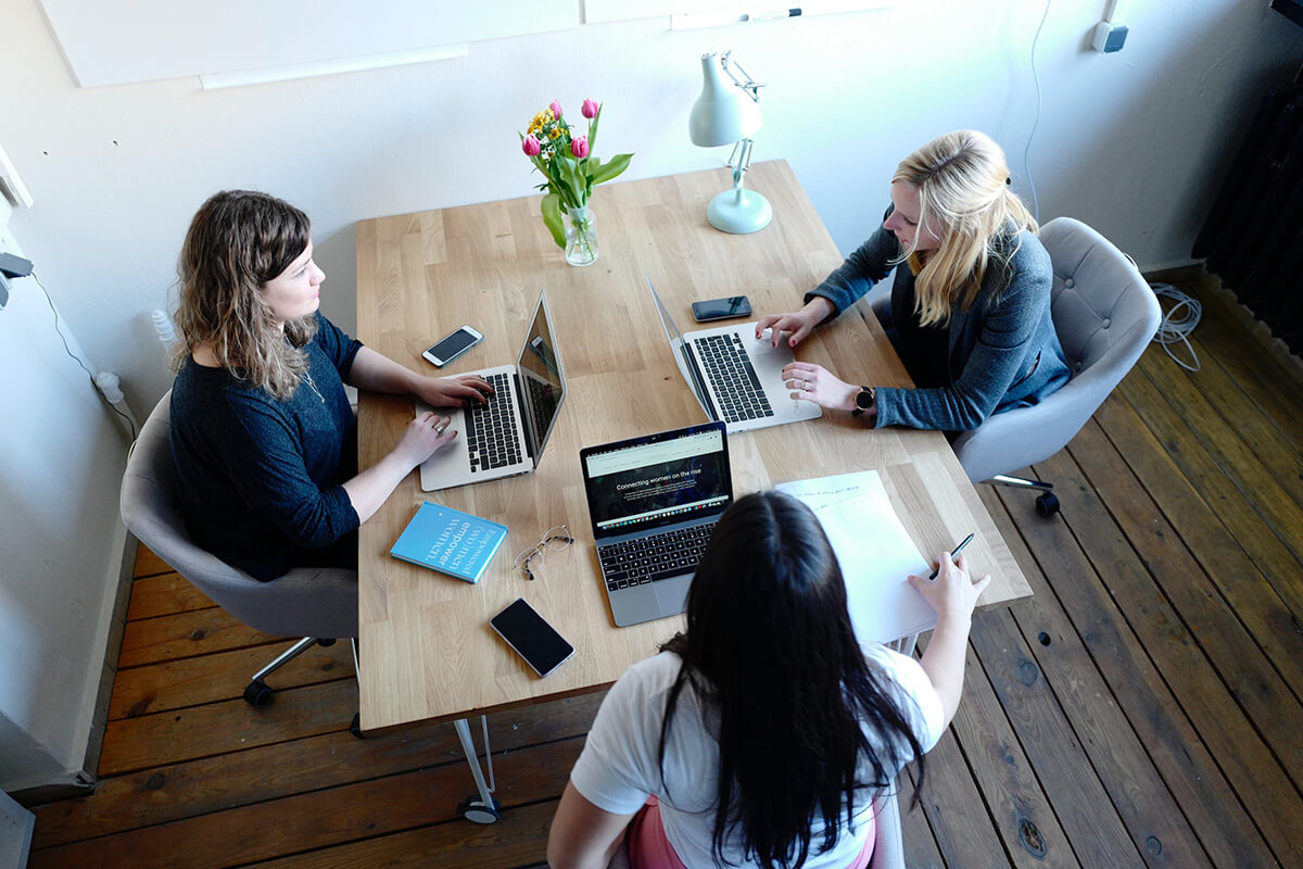 3 women working around a wooden table in a small office